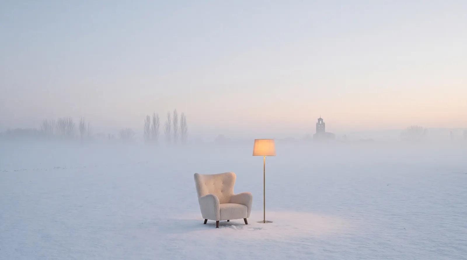 Un sillón de lana y una lámpara encendida, solos en una llanura nevada al amanecer, con un pueblo al fondo entre la bruma